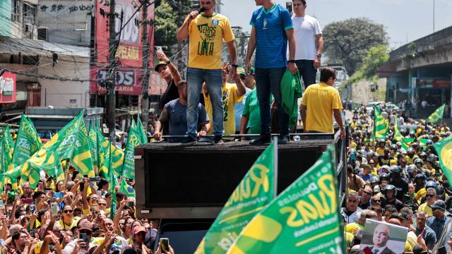 Homem de camisa amarela com microfone em cima de um trio el&eacute;trico, rodeado por outros homens e bandeiras verdes e amarelas, em meio a uma multid&atilde;o em manifesta&ccedil;&atilde;o na rua